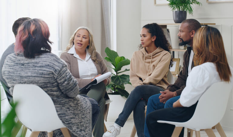 A diverse group of clients holding a group therapy with a female community support worker