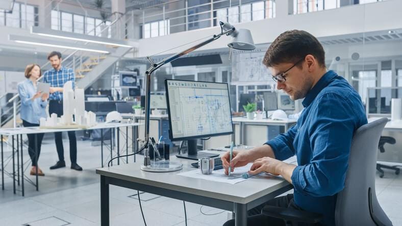 A process piping designer working on plant drafting plans in an office